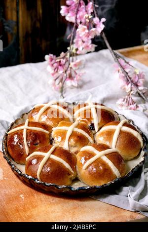 Homemade Easter traditional hot cross buns on ceramic dish with blossom flowers over orange stone table with linen cloth. Easter holiday baking Stock Photo