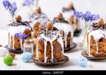 Homemade traditionla small Easter kulich cakes with chocolate nests and eggs on plates decorated with muscari flowers over white background. Tradition Stock Photo