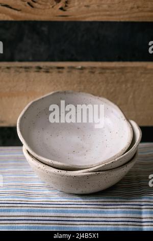 Set of empty craft ceramic white speckled bowls in stack standing on wooden shelf. Stock Photo