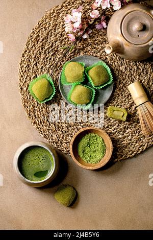 Asian rice dessert sweet green matcha mochi with cup of frothed matcha tea and green matcha powder in ceramic plate on brown table. Teapot and spring Stock Photo