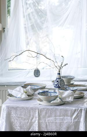 Elegant Easter table setting with empty painted porcelain tableware, plates and bowls, Easter eggs decorations, branches in vase on white tablecloth i Stock Photo