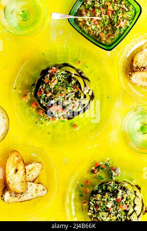 Steamed Artichokes with Italian Salsa Verde on a bright yellow background Stock Photo