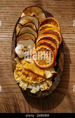 Top view of thin slices of dried fruit, pineapple, apple and orange, on a small wooden tray, on a wooden table Stock Photo