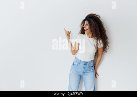 SEASONAL SUMMER SALE OFFER CONCEPT. Enjoyed pretty curly Latin female smiling, look up, hold hand up, show copy free space. Cool offer for ad. Studio Stock Photo