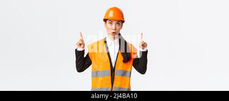 Building, construction and industrial concept. Surprised and curious asian female construction manager, engineer in safety helmet and reflective Stock Photo