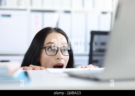 Young businesswoman peering over her desk in office in wide eyed horror or amazement Stock Photo