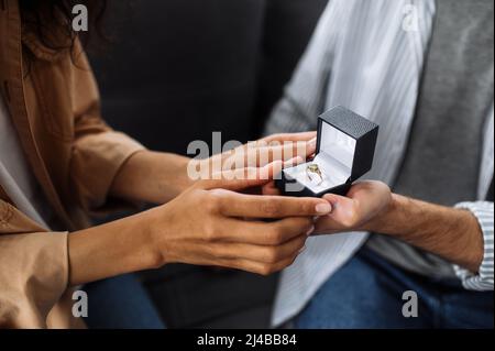 Close-up photo of an caucasian man gives an engagement ring to his beloved african american woman, she gladly accepts it Stock Photo