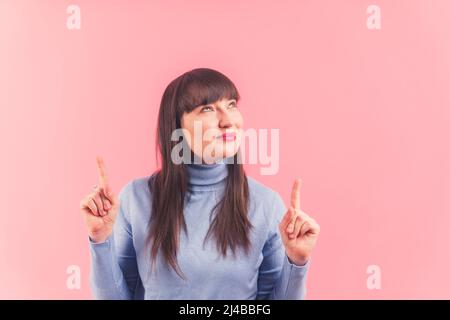 Pretty young woman points and looks above, studio shot pink background isolated copy space ads and promotion concept . High quality photo