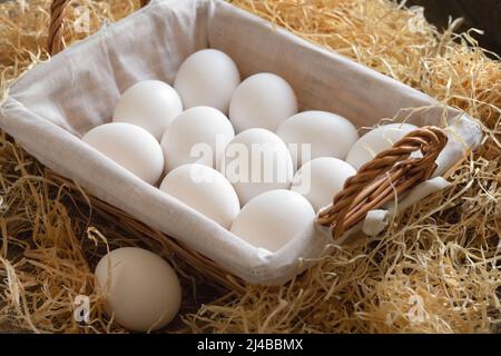 Wicker basket full of white chicken eggs on a hay Stock Photo