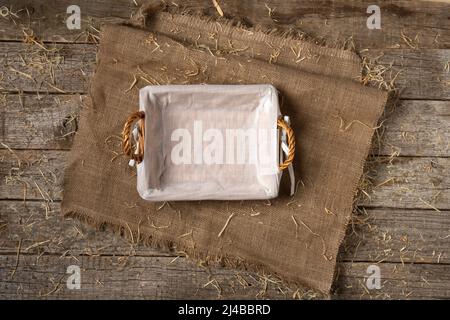 Empty wicker bread basket with white napkin on burlap cloth covered with straw Stock Photo