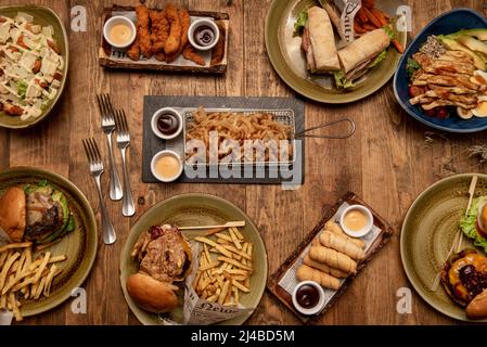 Set of plates with beef burgers with melted cheddar cheese, onions, pickles, bacon and many homemade fries, sandwiches, chicken pieces, fried onion ri Stock Photo