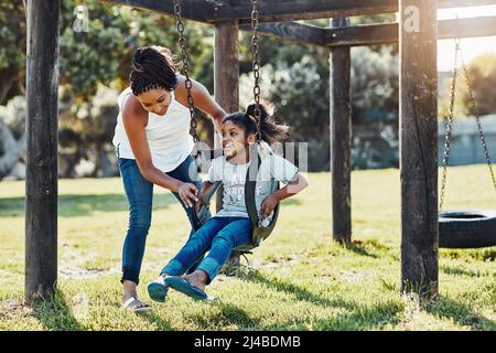 Out for some sun and fun. Full length shot of a mother pushing her daughter on a swing at the park. Stock Photo