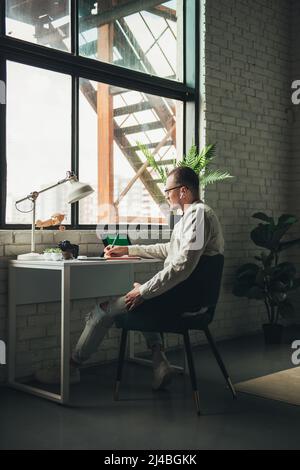 Businessman sitting at a table with tablet, writing on paper. Distance education. Marketing concept. Communication technology. Stock Photo