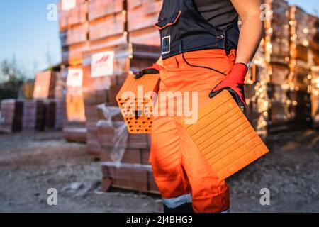 Close up on hands and midsection of unknown man construction worker taking orange hollow clay blocks ar warehouse or construction site in sunny summer Stock Photo