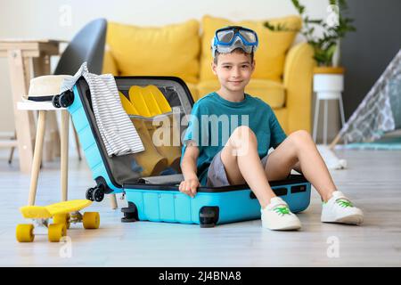 Cute little boy with snorkeling mask and belongings sitting in suitcase at home Stock Photo