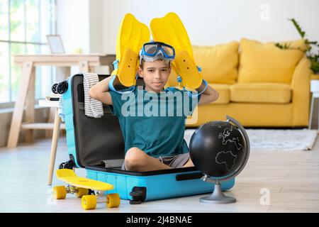 Funny little boy with snorkeling mask, paddles and globe sitting in suitcase at home Stock Photo