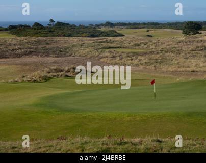 Red flag at a hole at the Bandon Dunes Golf Resort in coastal Oregon with the Pacific Ocean in the background and green in the foreground. Stock Photo