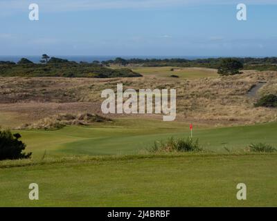 Flag at a hole at the Bandon Dunes Golf Resort in coastal Oregon with the Pacific Ocean in the background and green in the foreground. Stock Photo