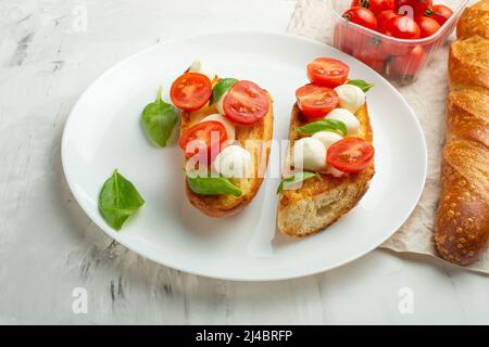 Bruschetta with tomatoes, mozzarella cheese and basil on a light background in a white plate. flat lay Stock Photo