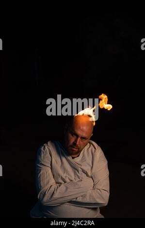 Bald man in a straitjacket with a burning head on a dark background. Stock Photo