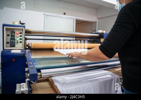 A worker printing on t shirt in workshop. clothing industry concept. Heat transfer machine. Stock Photo