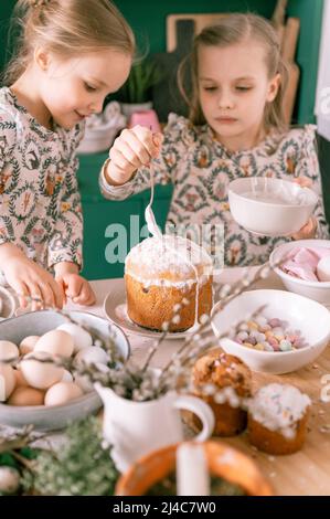 happy family candid little kids sisters girls together have fun ready springtime Easter holiday at home in kitchen decorating table and Easter cakes b Stock Photo