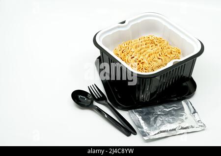 Instant noodles in a black plastic bowl with black plastic spoon and fork, ingredients in a small folie pack, automatic heat instant noodle soup by po Stock Photo