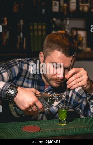 Bartender pouring tequila down spiral stem of bar spoon into shot glass with banana liqueur Stock Photo