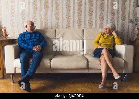 Elderly upset married couple sitting apart on leather sofa in their old-fashioned apartment after a quarrel. High quality photo Stock Photo