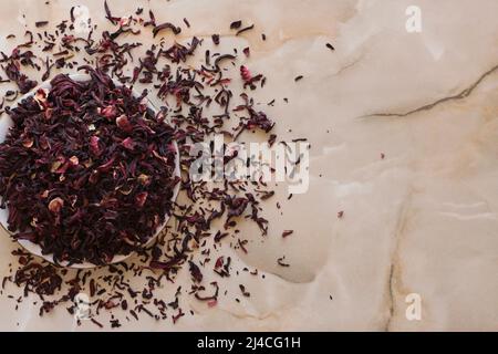 Dry hibiscus tea in a bowl. Dried hibiscus calyces, herbal tea made of crimson and deep magenta-colored sepals of the roselle flower, in the bowl on t Stock Photo