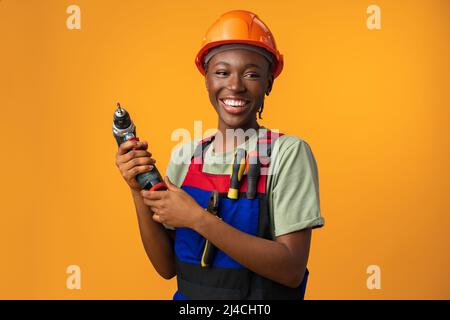 Smiling young african american woman in hardhat holding screwdriver tool in studio Stock Photo