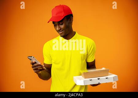 African delivery man wearing courier uniform holding cardboard parcel using smartphone Stock Photo
