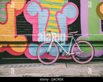 Shoreditch, London, UK - April 14, 2016: Colourful East London street art, with an equally colourful bicycle resting against it. Stock Photo
