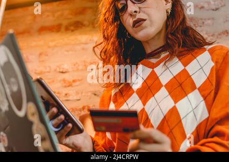 Caucasian young woman sitting shopping online with a credit card, phone and a laptop, online trading concept, copy space. Stock Photo
