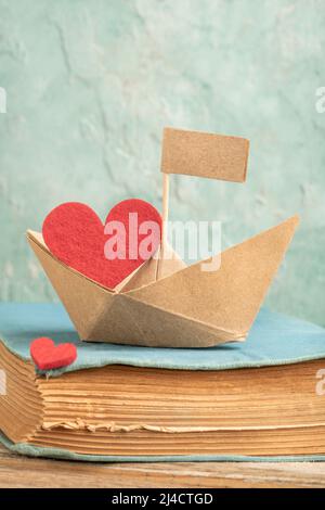 origami paper boat on an old book on table isolated green background or surface. Hand crafted origami paper sailing boat on book decorated with red he Stock Photo
