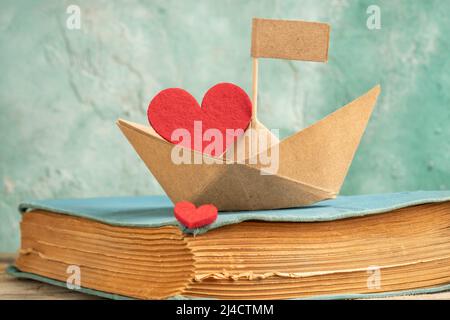 origami paper boat on an old book on table isolated green background or surface. Hand crafted origami paper sailing boat on book decorated with red he Stock Photo