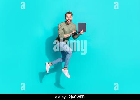 Full length photo of crazy freelancer man jump hold netbook run wear pullover isolated blue color background Stock Photo