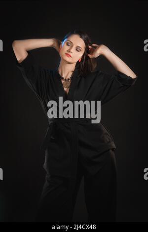 Studio shot in low key with woman with raised hands in black clothes. Stock Photo