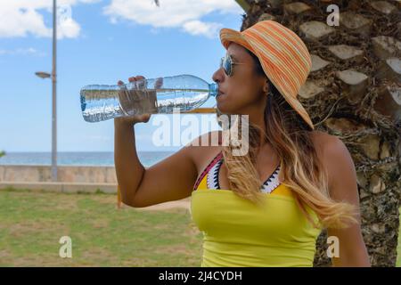 Happy woman drinking mineral water next to a palm tree enjoying the summer. Copyspace. Stock Photo