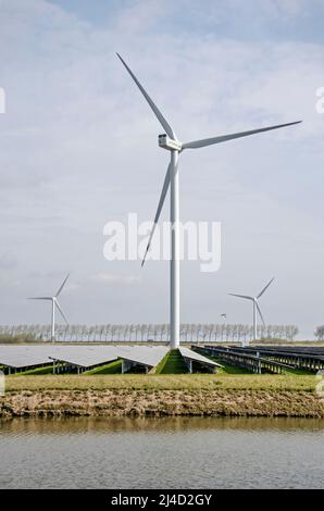 Middelharnis, The Netherlands, March 30, 2022: view across a field of solar panels, one large wind turbine and two more turbines in the distance Stock Photo