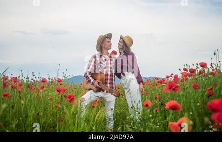 Man and woman embracing and kissing in poppy field on the dusk with guitar, music Stock Photo