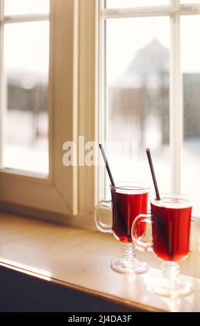 Two glasses of mulled wine on the windowsill overlooking the winter mountains. Winter hot drink Stock Photo