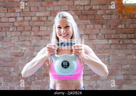 Young attractive blonde fitness woman is doing exercise with a kettlebell workout. Sporty girl showing her well trained body. isolated on brick wall background with copyspace. High quality photo Stock Photo