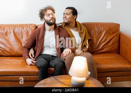 Male gay couple talking on a couch at home Stock Photo