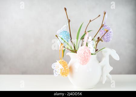 Home interior with easter decor. Vase with willow tree branches with Easter eggs and bunny on white table and background with copy space Stock Photo