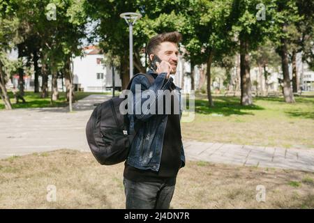 Young man travels, about to set off with a full backpack, man in denim jacket talking on the phone, a backpack stuffed to the brim Stock Photo