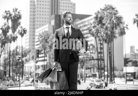 confident man in elegant suit walk with shopping bags and giftbox outside, purchase Stock Photo