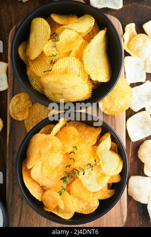 Potato corrugatedchips. Fast food. Crispy potato chips ceramic black bowl with sour cream sauce and onions in wooden stand on old kitchen table wooden Stock Photo