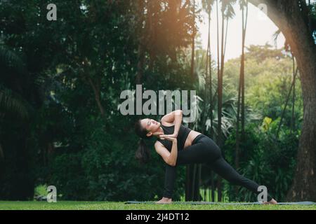 asian woman practicing yoga in prep poses for side crane pose for parsva bakasana on the mat in outdoor park 2j4dt12