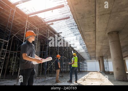 Architect, Engineer, Contractor, or Construction manager holding digital tablet standing with a group of worker at a construction site. Stock Photo